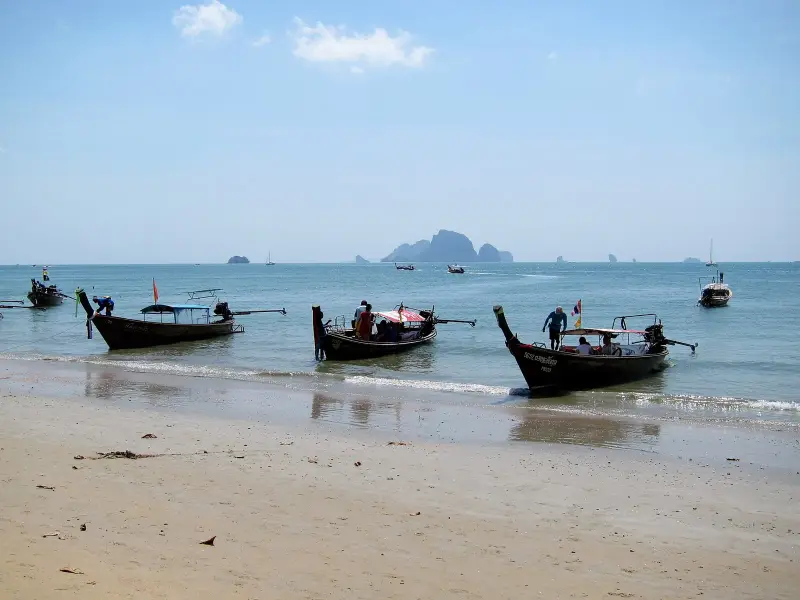 Longtail boats at the water's edge on Ao Nang beach with rocky islands in the distance
