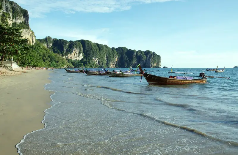 Ao Nang beach with longtails along the shore and limestone cliffs on the right