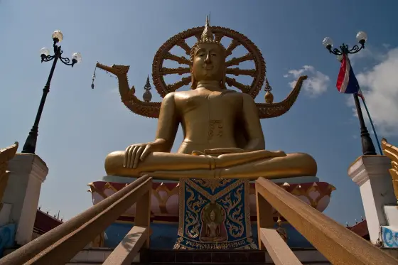 The golden Big Buddha on Samui with a Dharma wheel and barge prows behind it, seen from the stairway
