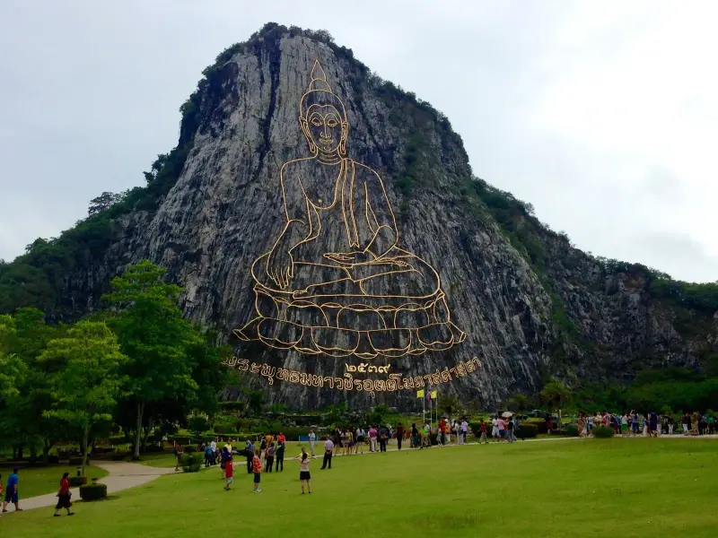 Golden outline of a seated Buddha on the sheer Khao Chi Chan cliff, with a lawn and visitors below