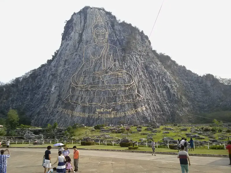 The plaza at the foot of the cliff, visitors photographing the golden image