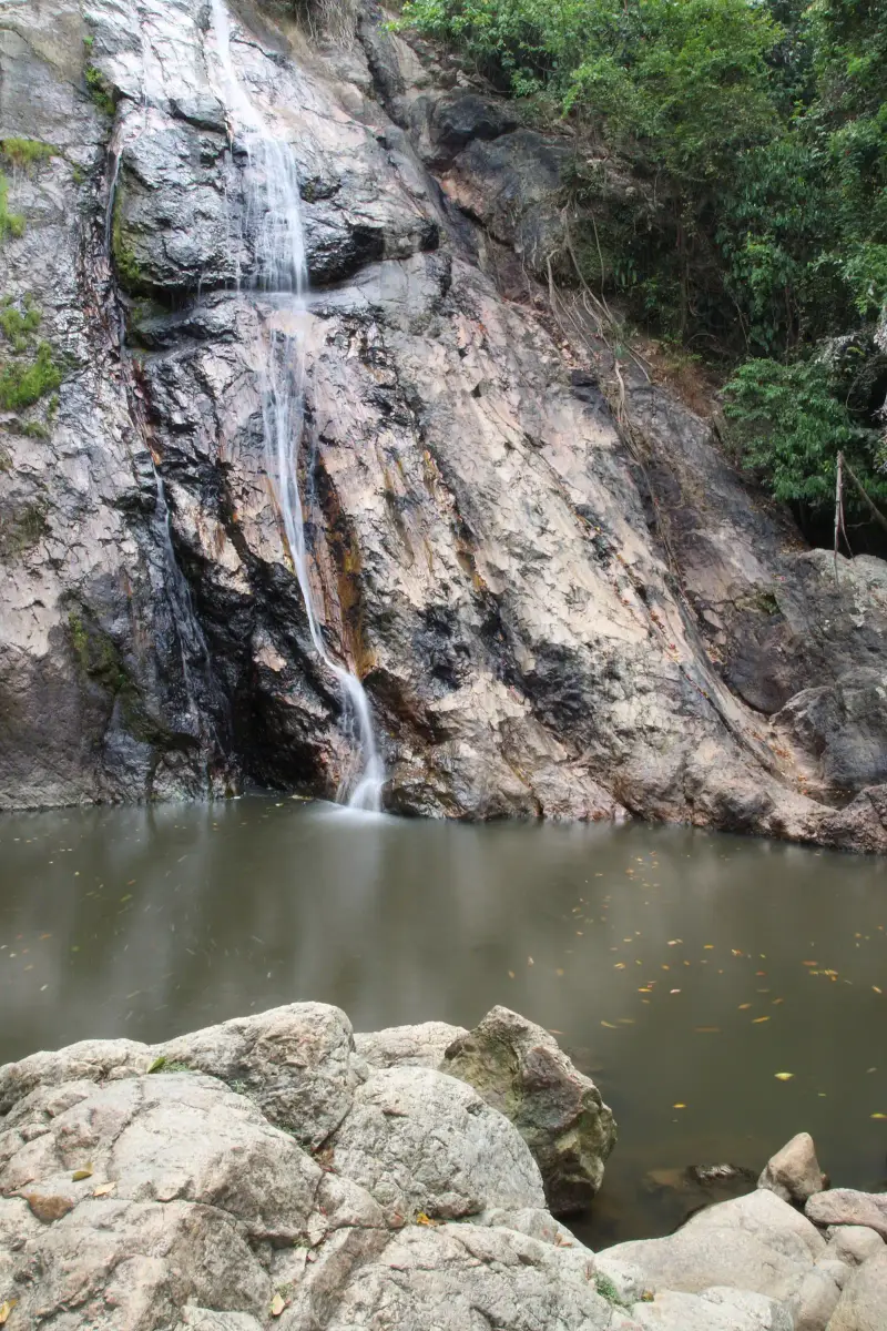 A thin stream of the Na Muang waterfall above a natural pool among rocks