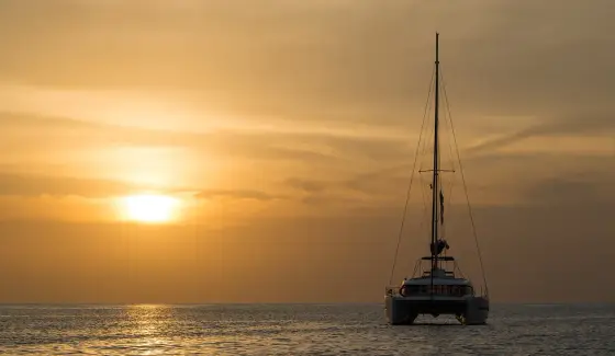 Парусный катамаран на якоре в море на закате, солнце над горизонтом