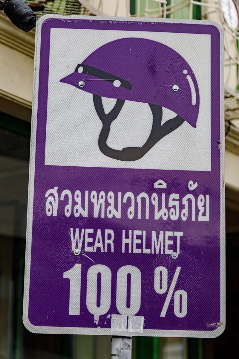 Purple road sign with a helmet and the words WEAR HELMET 100% in Phuket